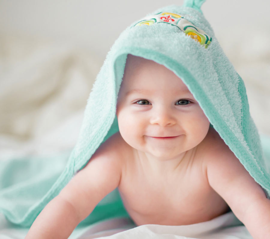Smiling baby, fresh from bath, with infant towel on their head