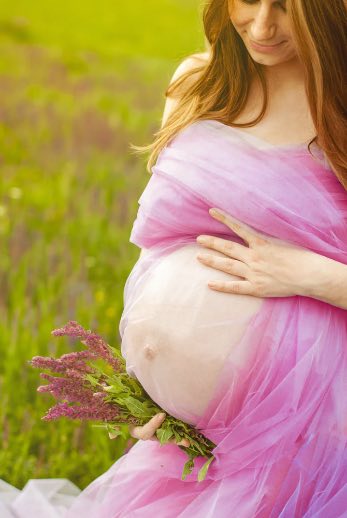 Pregnant woman wrapped in pink tulle, holding pink flowers